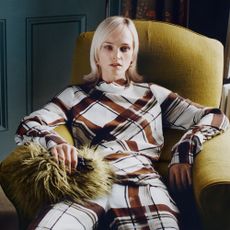 Model sat on green chair wearing a two piece plaid set sold at Harvey Nichols