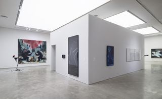 Art exhibition space with white walls with a central rectangular pod, displaying artwork on the walls of varying sizes.