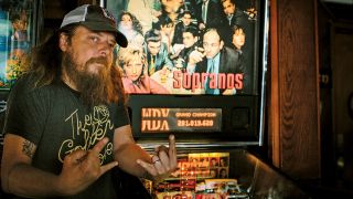 A photograph of Bryan Giles giving the horns next to a Sopranos pinball machine