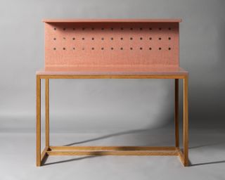 A light wood writing desk with a back that contains three rows of circular holes.