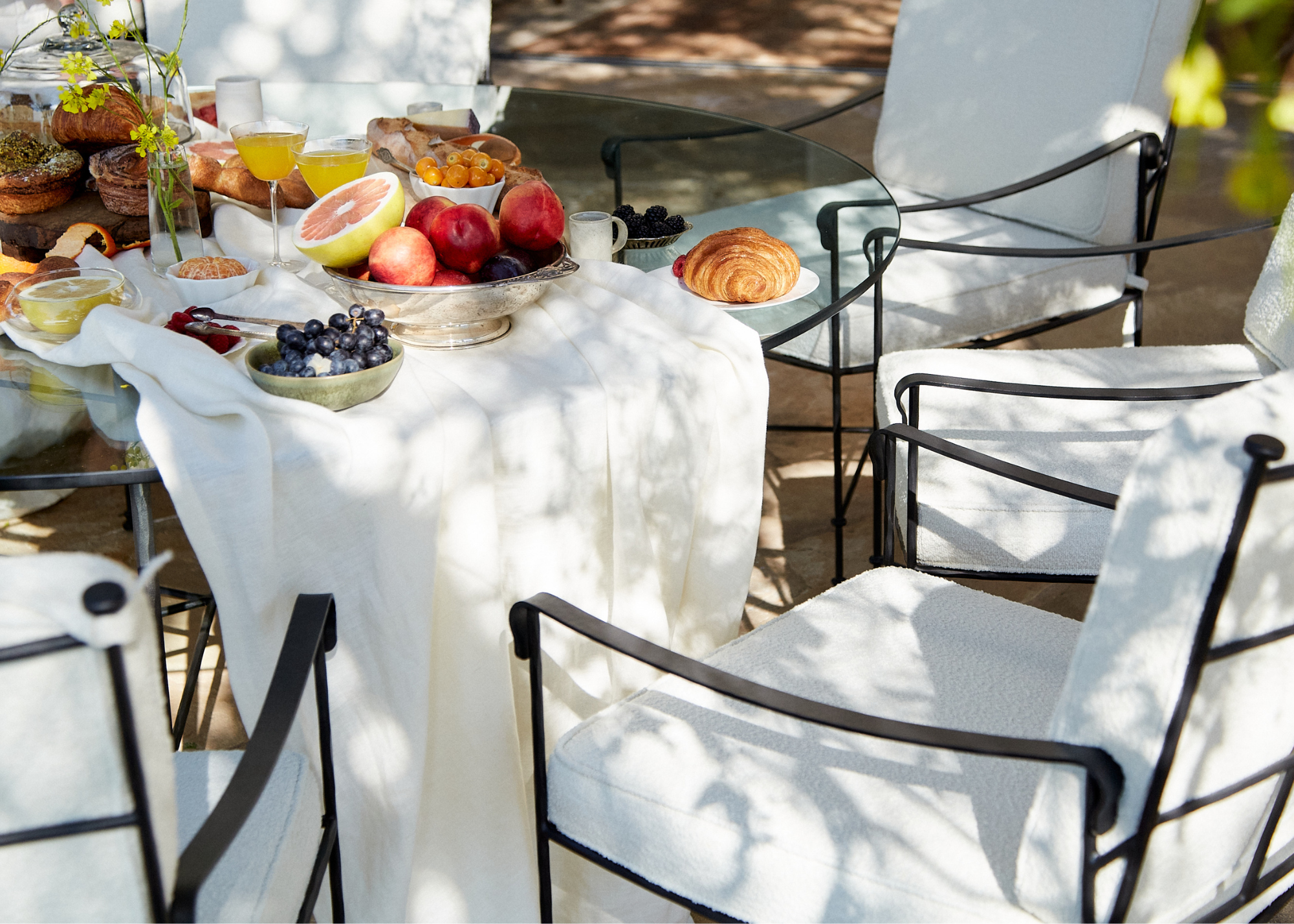 An outdoor garden with outdoor wrought iron table table and chairs with boucle seat detailing and textured table runner