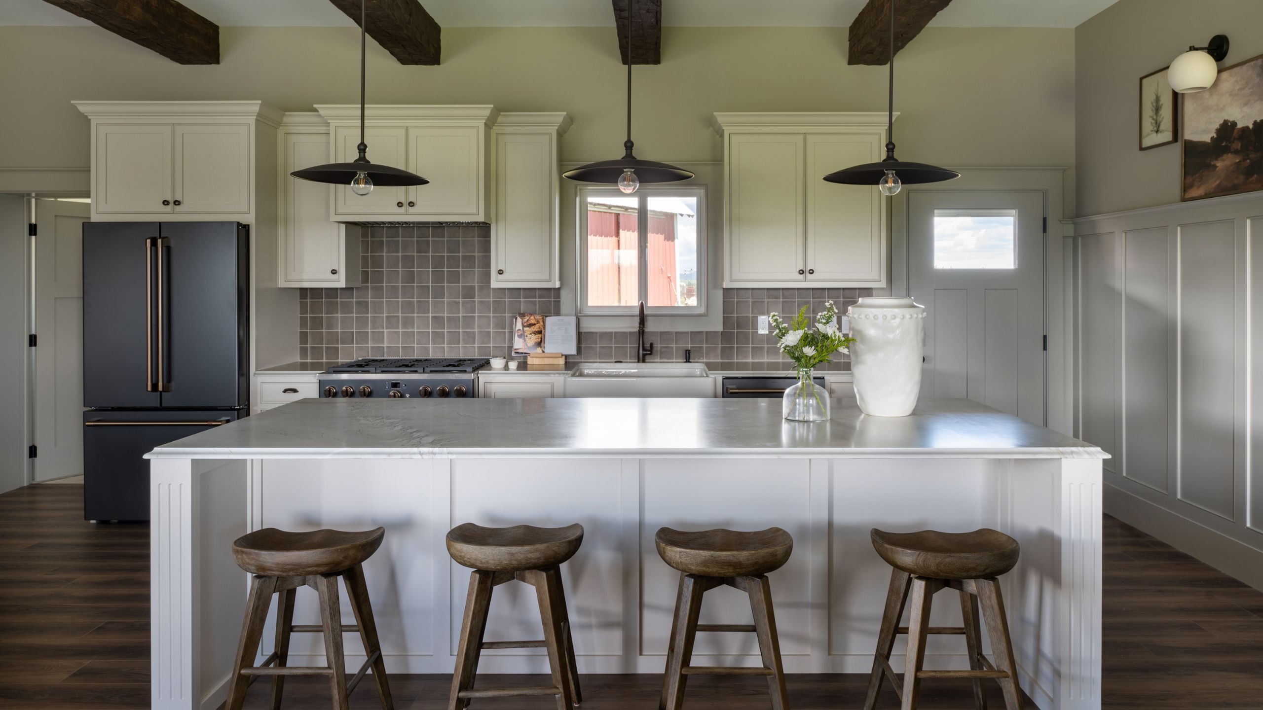 a moody neutral kitchen with soft white cabinetry and island, wooden floor, zellige tiles and ceiling beams