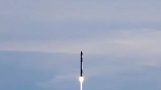 a white and black rocket launches into a blue sky.