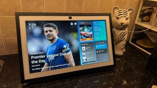 Amazon Echo Show on a counter displaying the home screen, with sports news alongside the widgets panel.