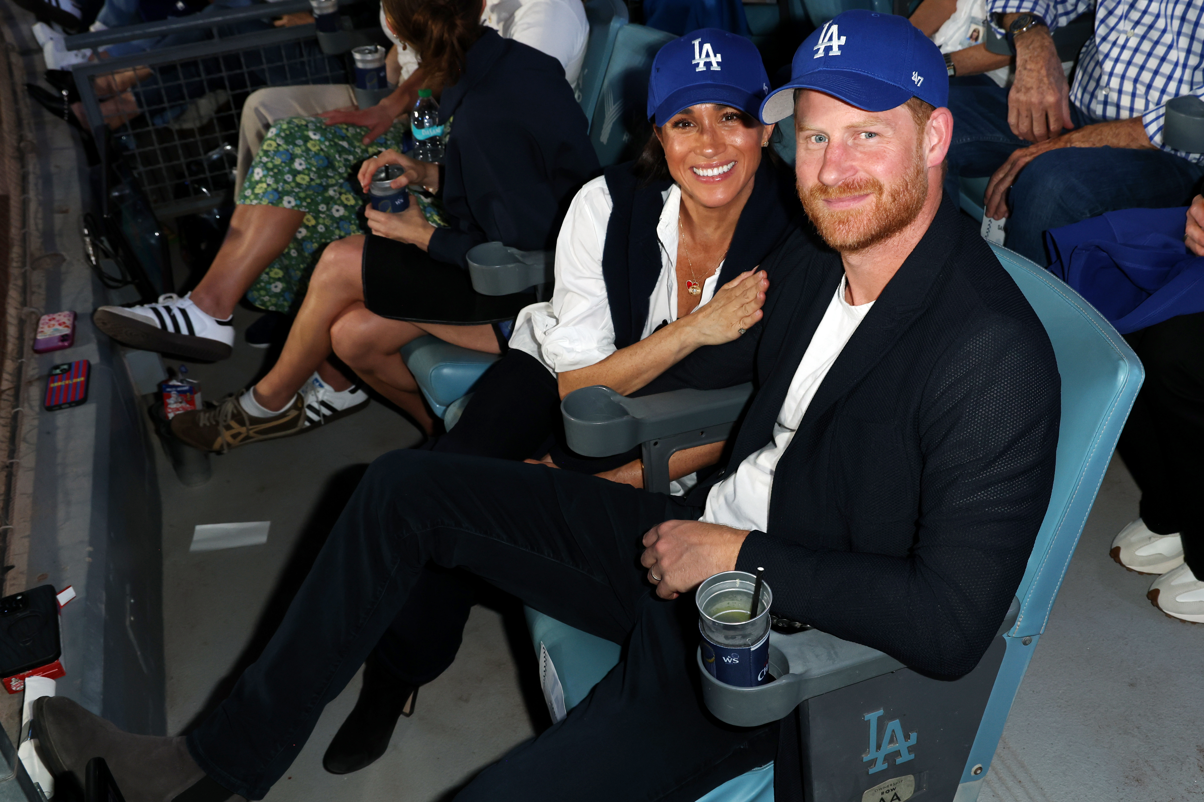 Meghan Markle and Prince Harry sitting in seats wearing Dodgers hats at the World series