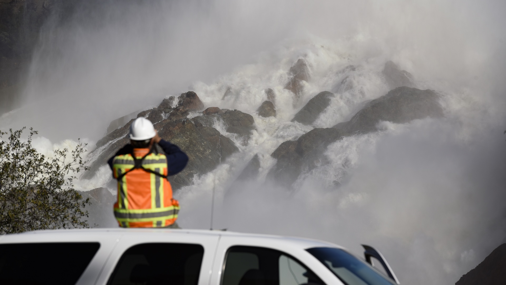 construction worker in orange vest and hardhat watches lots of water cascade down oroville spillway
