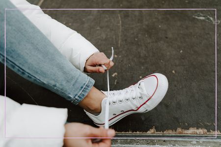 A woman tying up shoelaces on a white pair of Converse