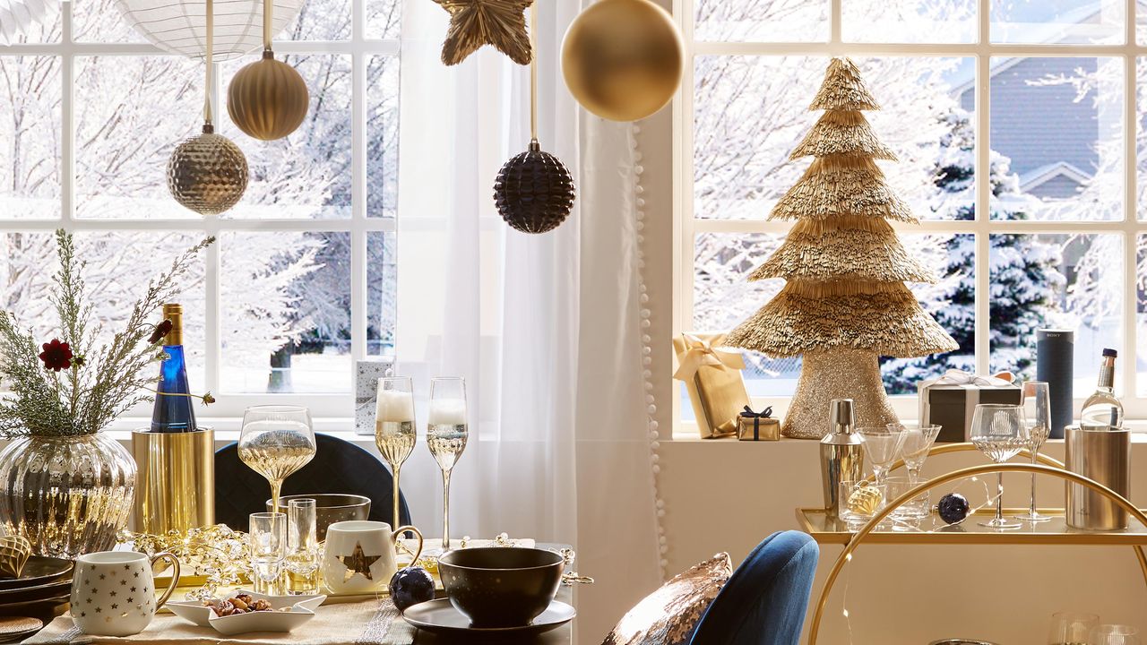 A gold and blue Art-Deco inspired festive dining area with straw Christmas tree in background above gold-framed bar cart