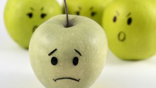 Cuatro manzanas con caras tristes pintadas que simbolizan la desaprobación de algunos consumidores.