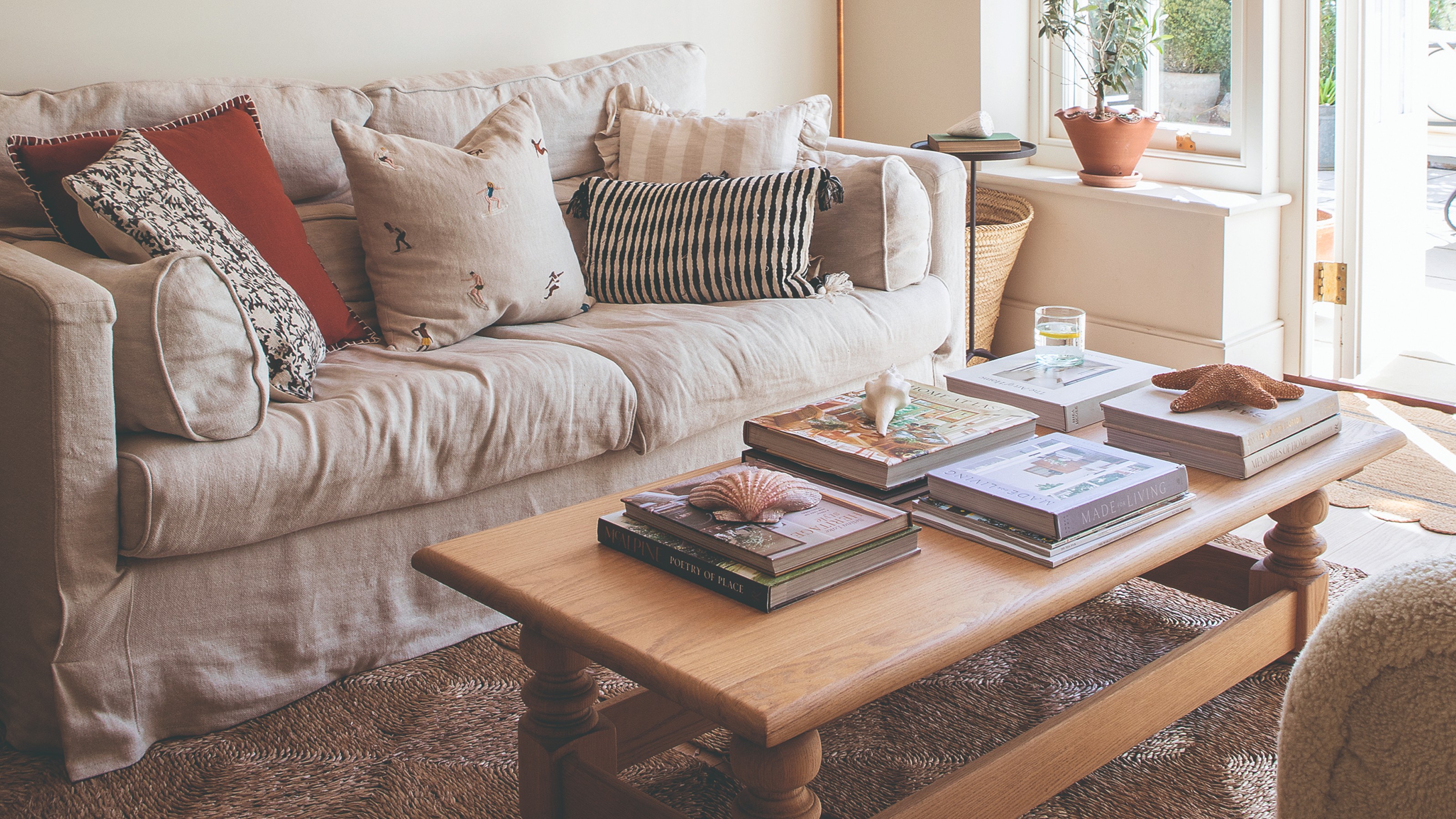 A bright living room with a cream loose cover sofa with mismatched scatter cushions