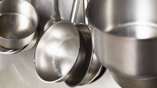 A close-up of stainless steel pots and pans hanging from a wall