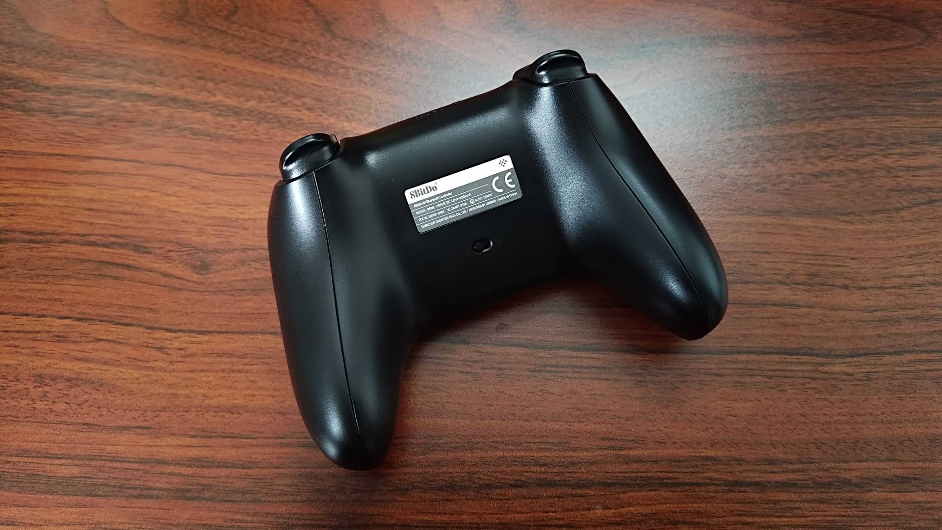 Back of 8Bitdo N64 Bluetooth controller sitting on woodgrain surface.