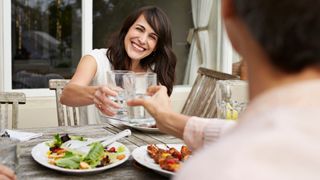 woman toasting with a glass of water as she eats dinner in the garden