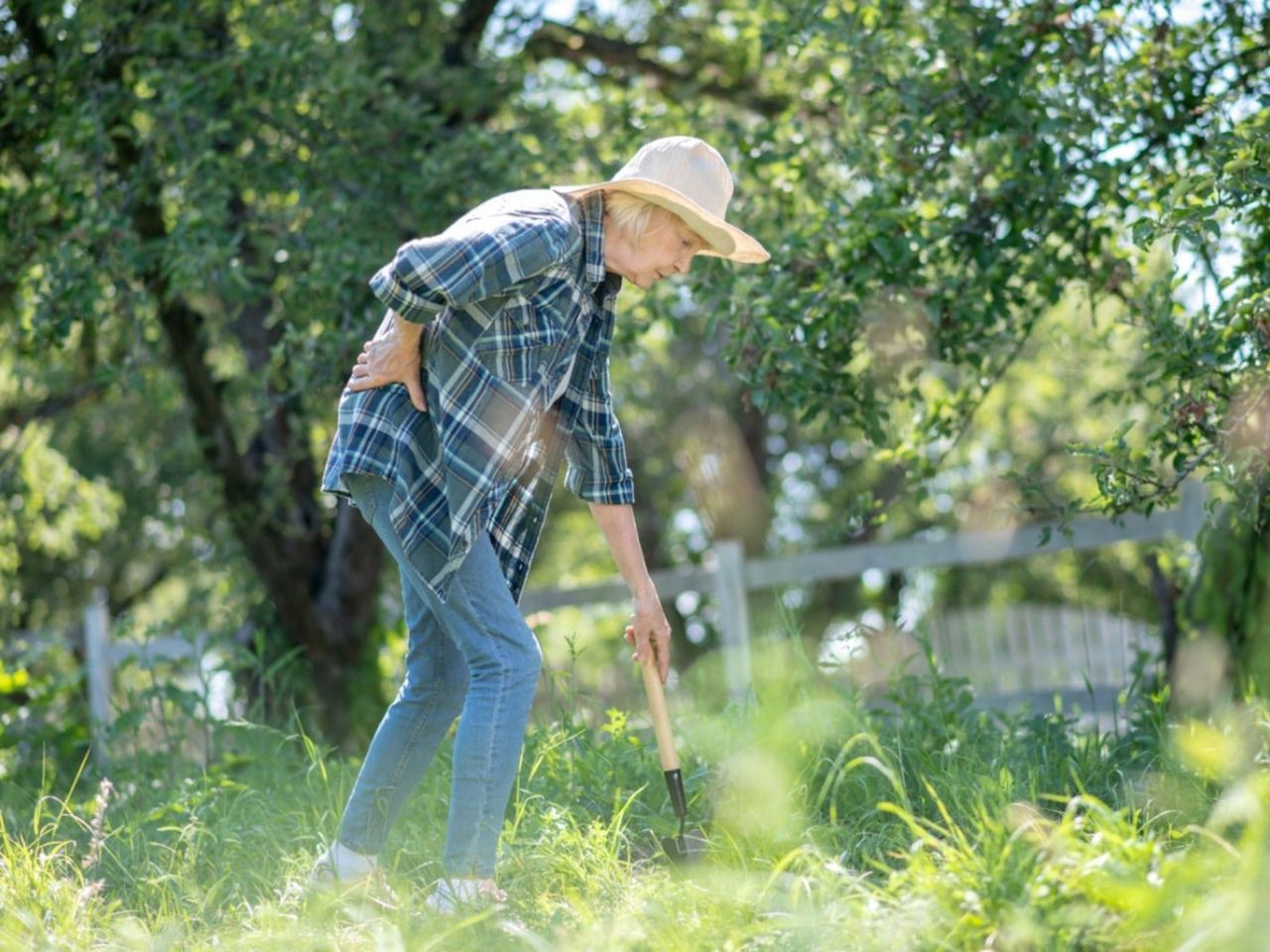 An older woman holds her back in pain while gardening