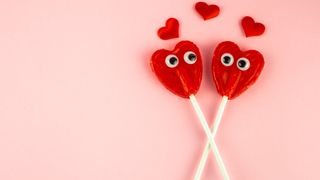 red heart lollypops with stick on eyes on pink background