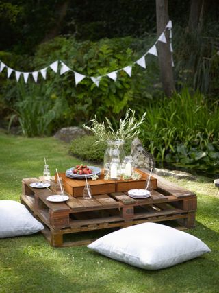 pallets used to make an outdoor dining area with bunting and outdoor cushions