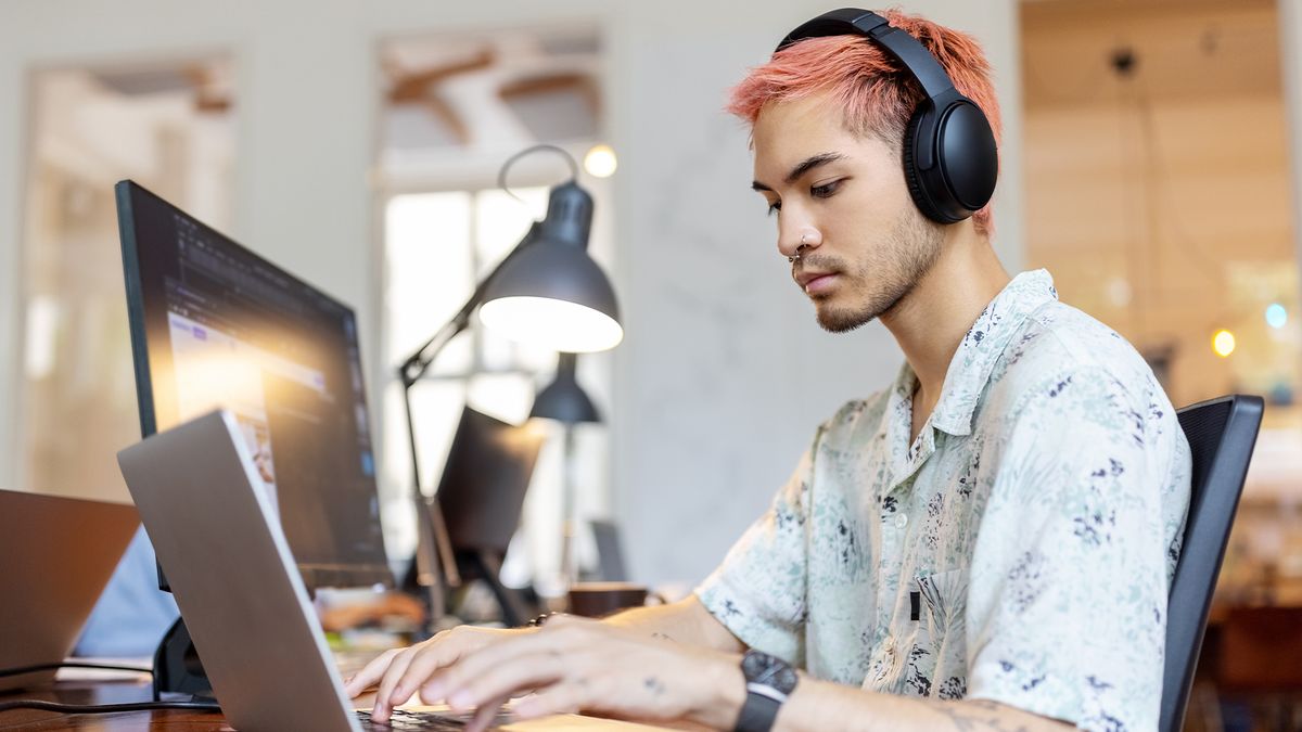 Male software developer coding in Swift programming language on a Macbook while sitting in an open plan office space.