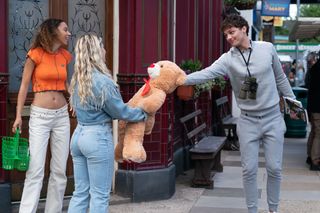 Freddie Slater and Anna Knight holding a giant teddy bear in front of the Queen Vic as Gina Knight looks on