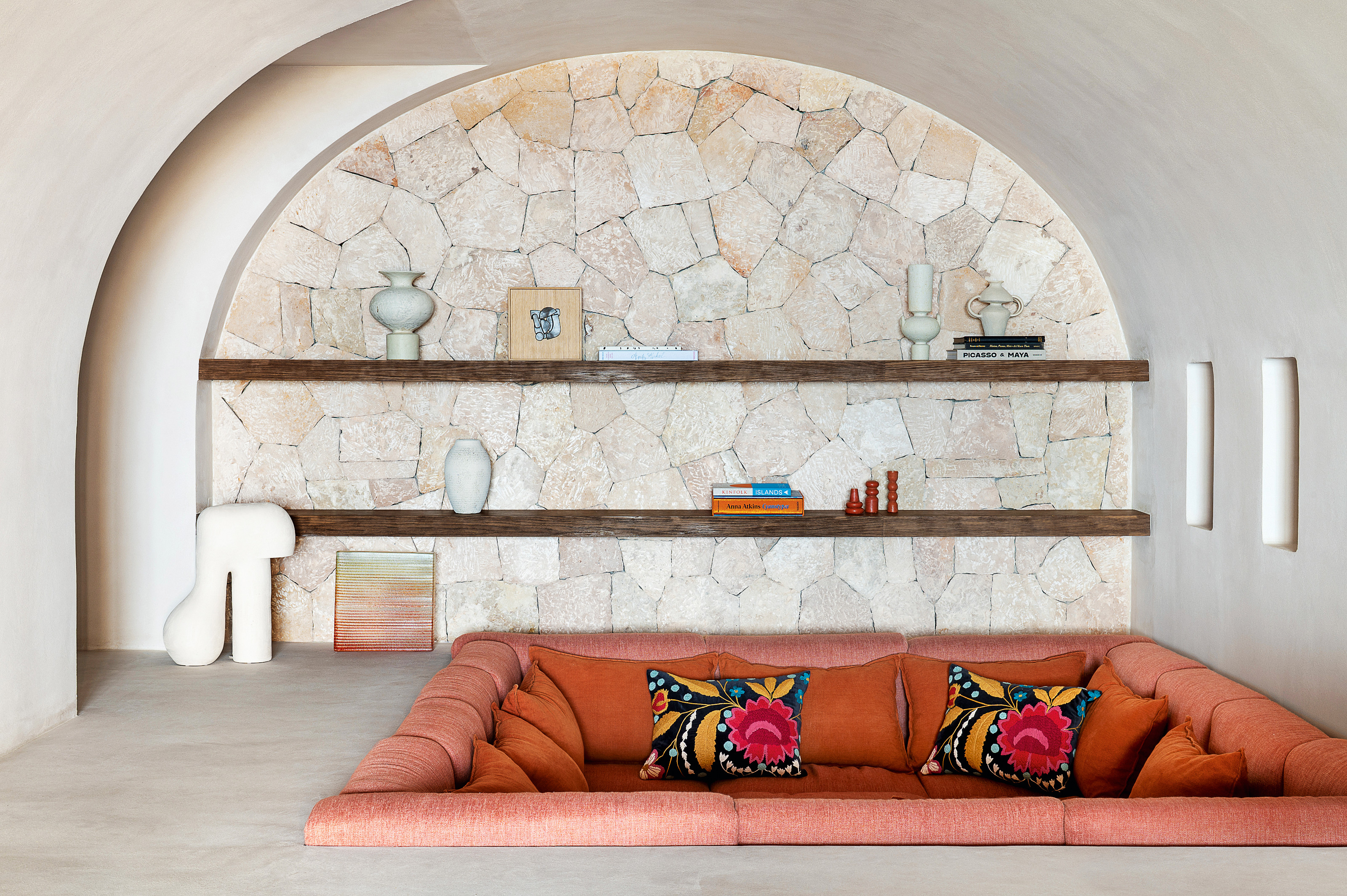 Terracotta-colored conversation pit set in an arched nook with white plastered walls and stone accents