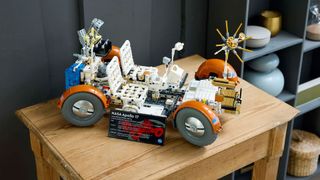 a white and orange four-wheeled lego rover sits on a small wooden table