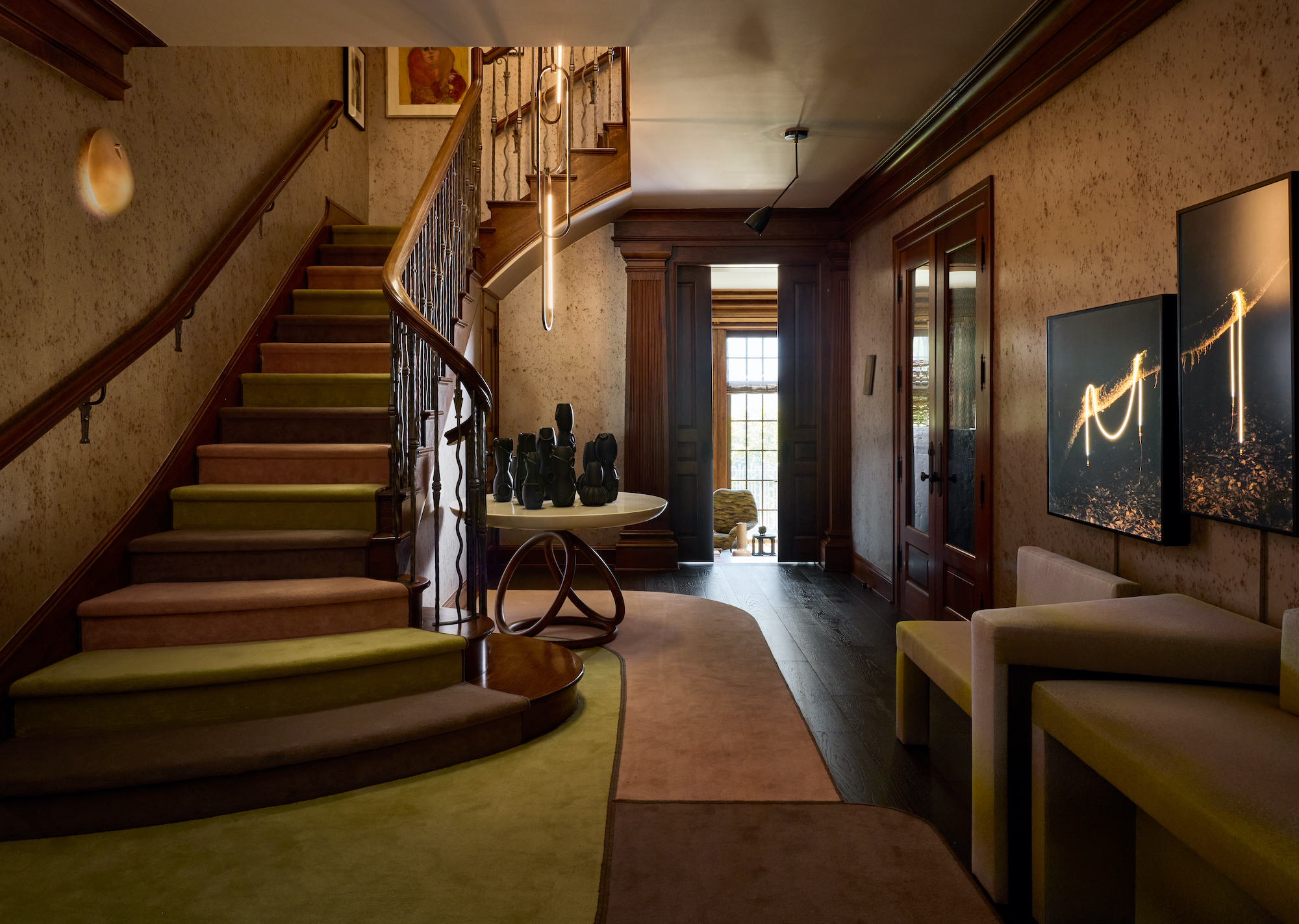 staircase with runner in different blocks of colour- greens and browns and hallway with seating and art