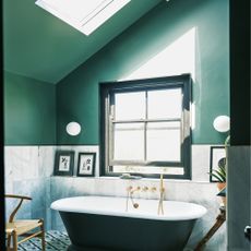 bathroom with green painted walls, grey tiles, black rimmed window and freestanding bath 