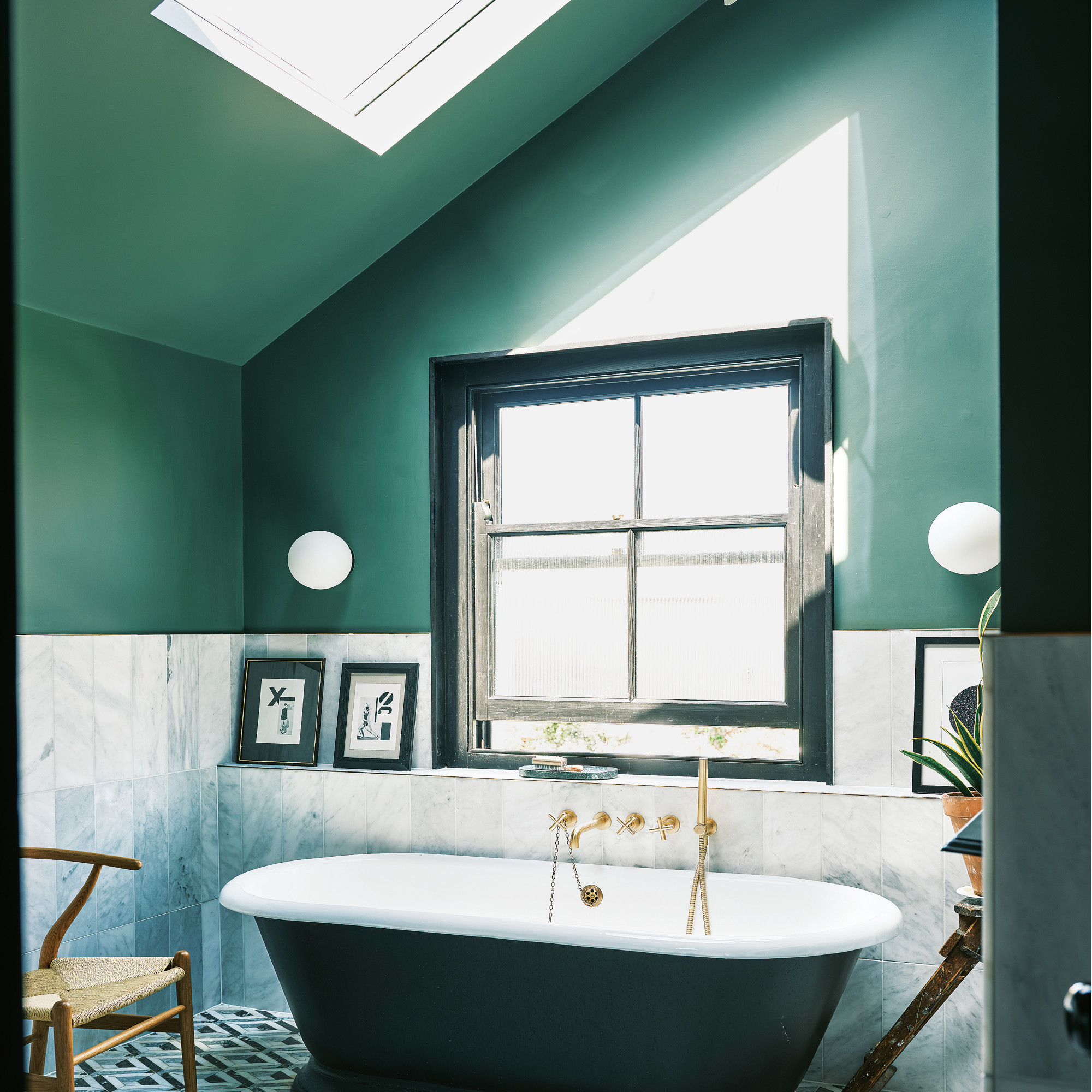 bathroom with green painted walls, grey tiles, black rimmed window and freestanding bath