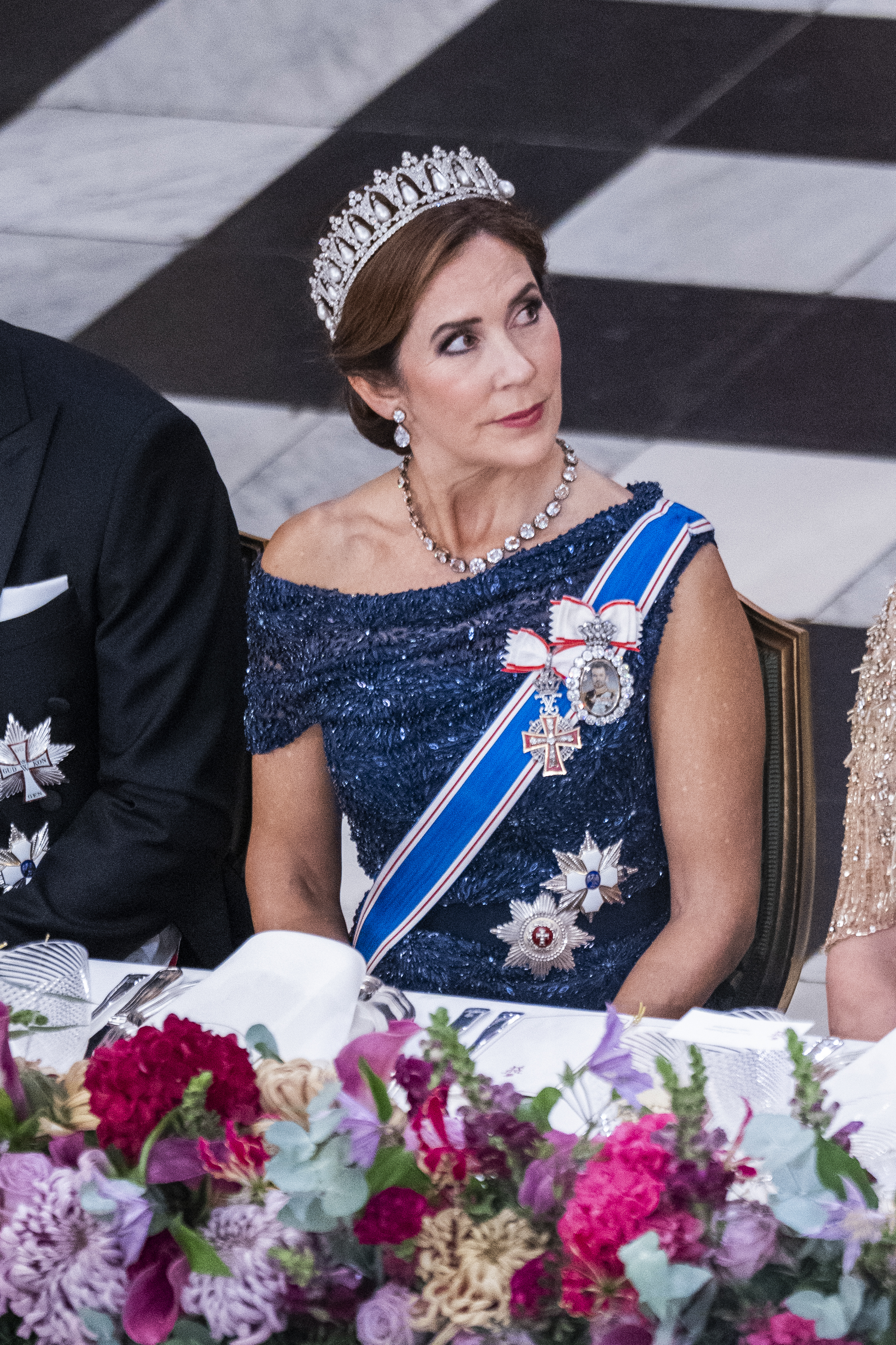 Queen Mary wearing a blue gown and a tiara sitting at a table