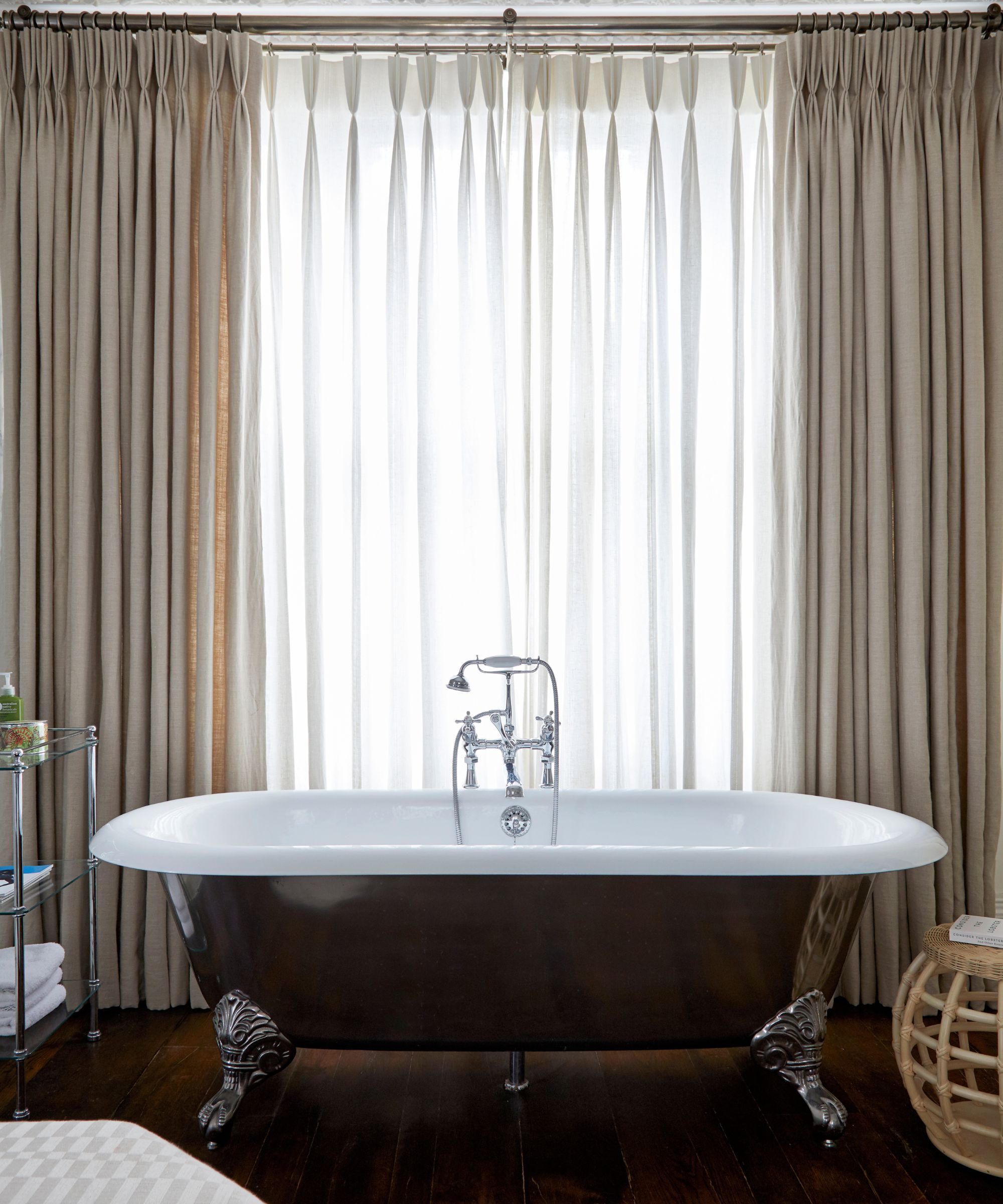 A bathroom with a black roll-top bath and sheer curtains behind.