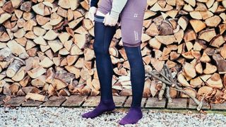 A man wears some cycling leg warmers in front of a stack of logs