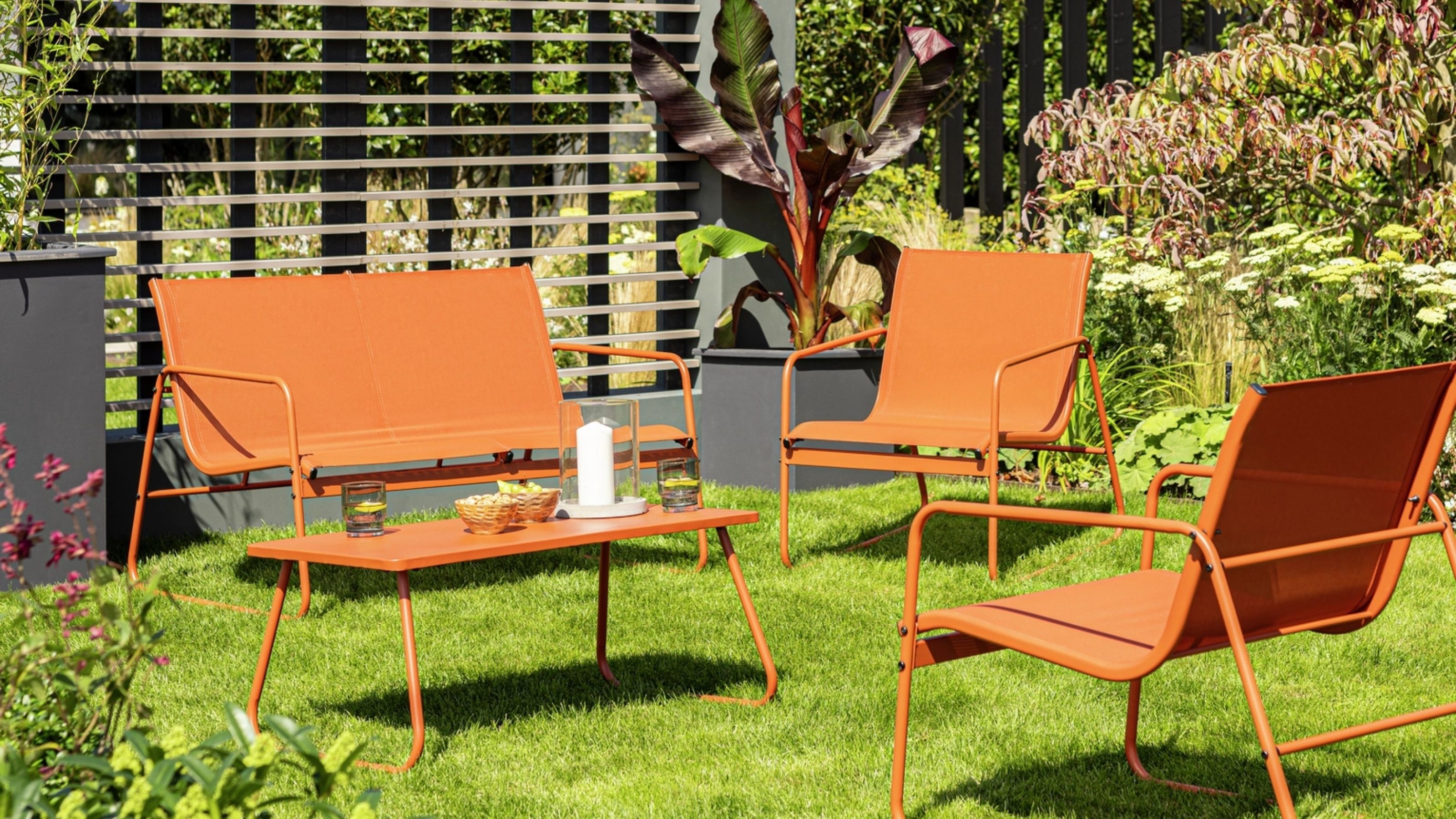 Image of an orange outdoor furniture set in a grassy backyard that has lots of plants.