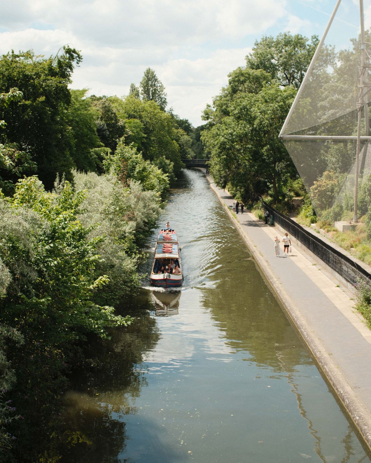 Boats sailing up a canal with next to a tow path with people walking