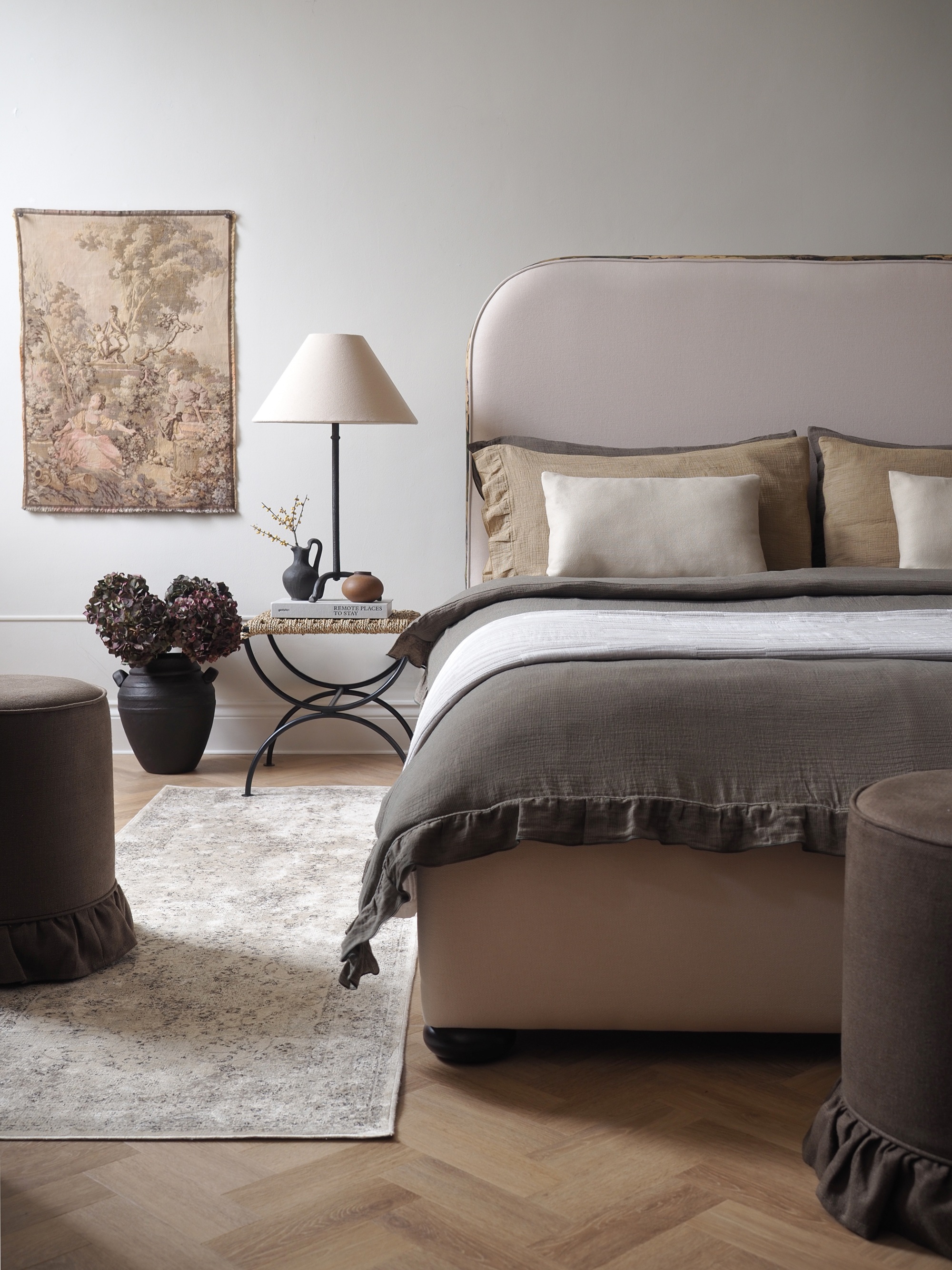 a white bed dressed with a dark throw, a patterned runner rug, and a tapestry on the wall
