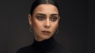 A woman in a black turtleneck and large circular earrings poses against a dark background, exuding elegance and confidence