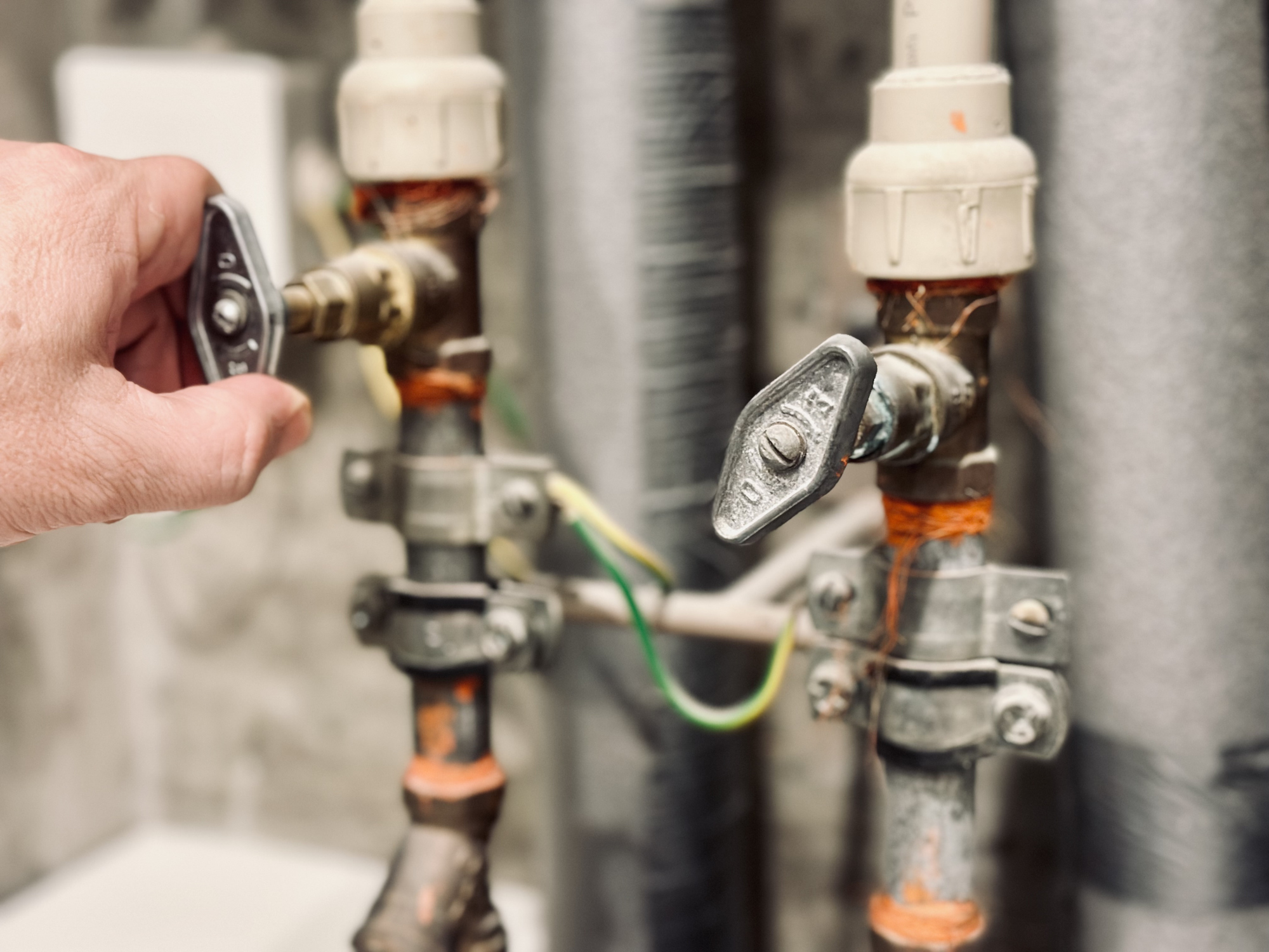 A man turning the water shut off valve on the pipe in his home.