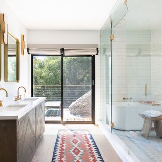 bathroom with neutral color scheme and brass taps with double basins and colored rug with picture windows overlooking green landscape