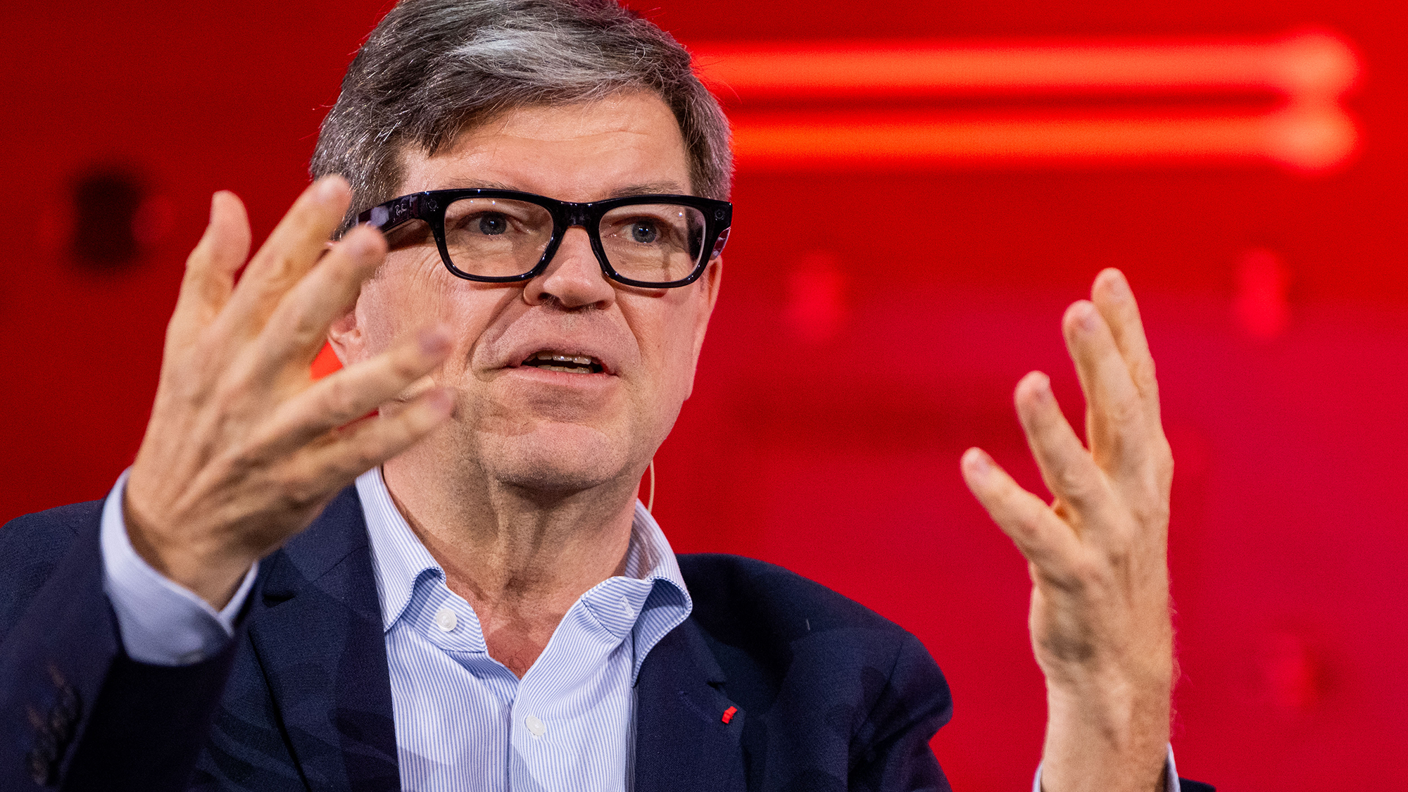 A man with gray hair and glasses speaks to an audience