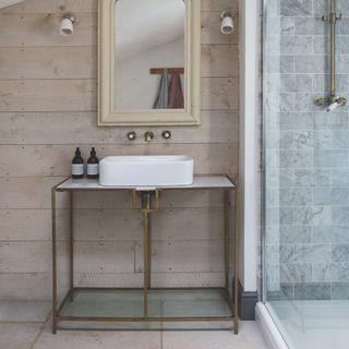 coastal style bathroom with metal vanity unit and sink, bare wood on walls, vintage mirror, wall lights, stone floor, shower to right