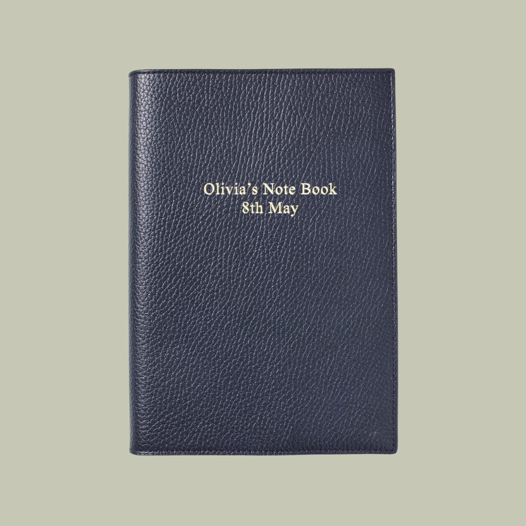 A5 Refillable Luxury Journal Navy Pebble with Soft Suede Lining against a pale green background reads "Olivia's Note Book 8th May" in engraved golden characters.