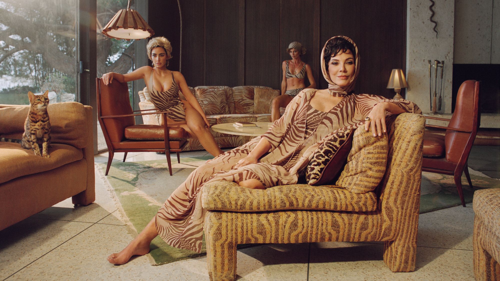 Roberto Cavalli x Skims campaign image of Kris Jenner lounging on a chair wearing a palm leaf-printed outfit and head scarf while Kim Kardashian sits on a chair in the back in a matching swimsuit.