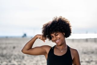 A woman on a beach flexing her bicep and winking