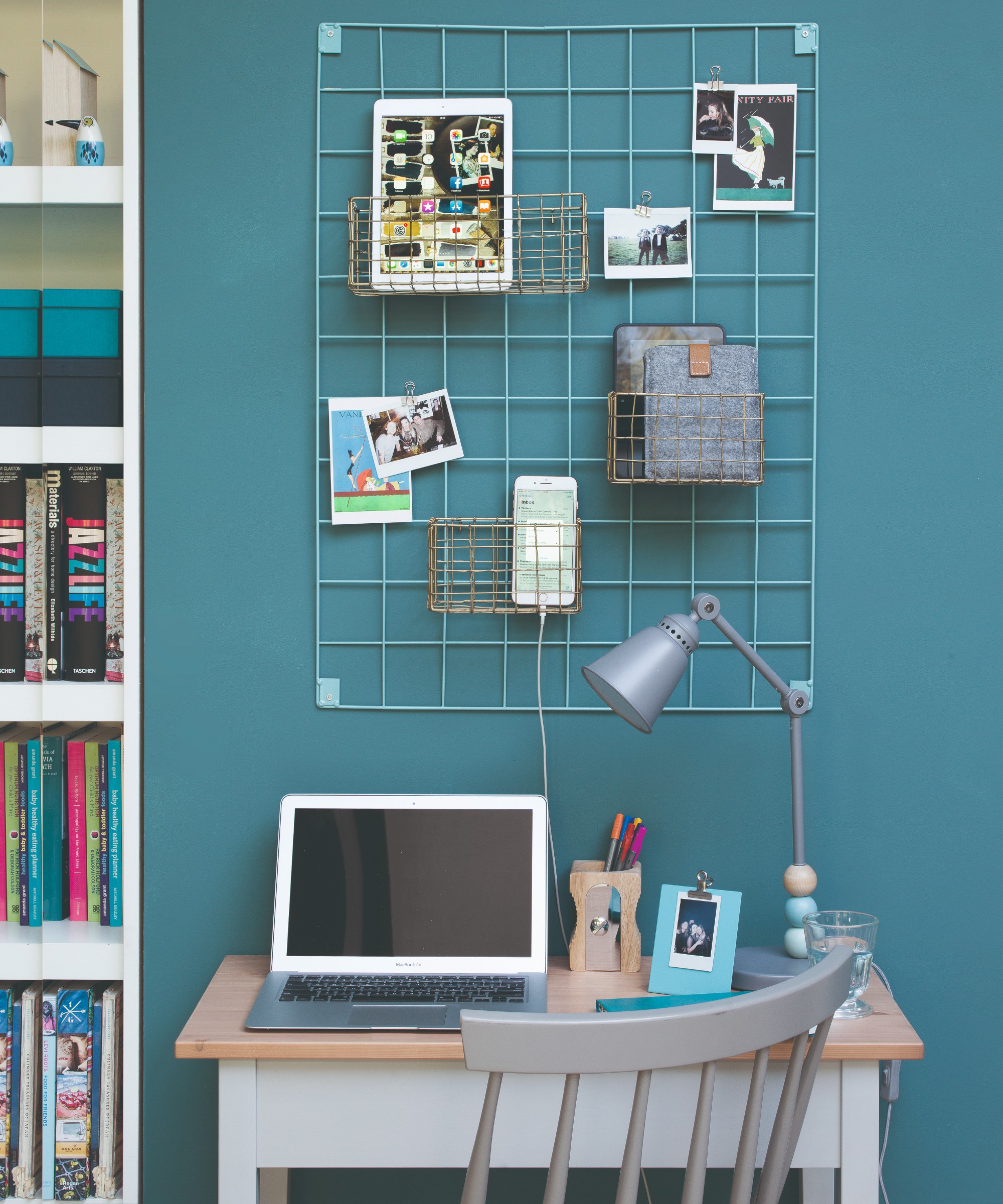 A desk with a laptop against a teal blue wall with an organisation board above holding a tablet