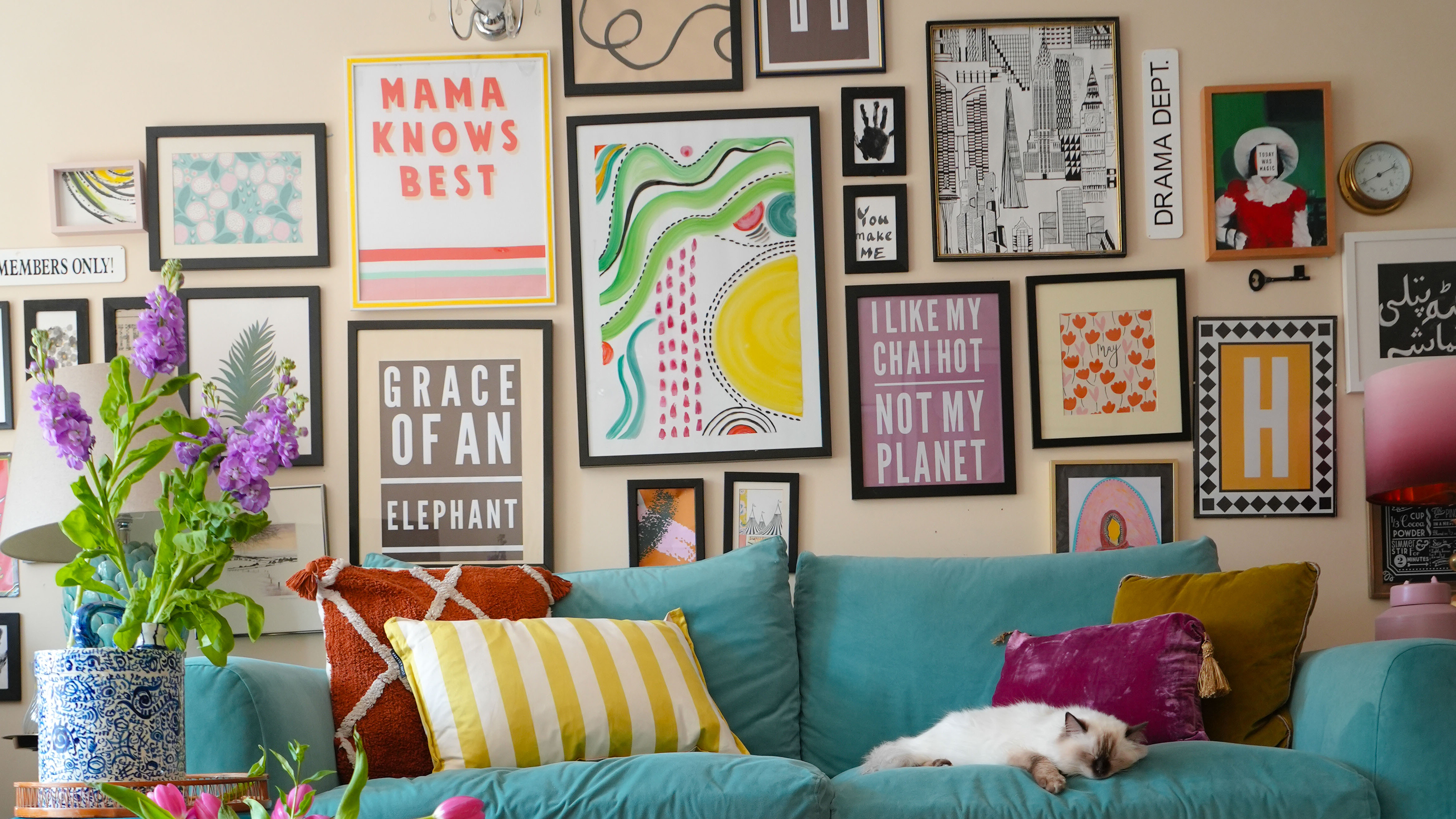 gallery wall full of art in an assortment of frames, arranged on a beige wall above a bright blue sofa