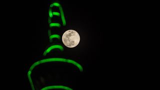 bright full moon of february in the center of the image and a tall minaret to the left illuminated by green lights.