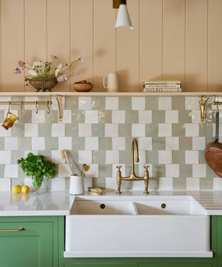 green kitchen with pale green and white zellige checkerboard backsplash, butler sink, and a pale pinky peach panelled wall and shelf above