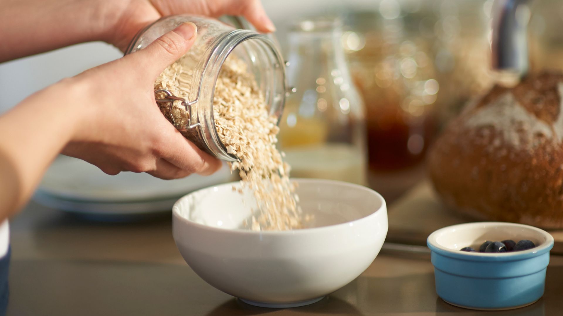 Woman's hands pouring oats into a ceramic bowl from glass container