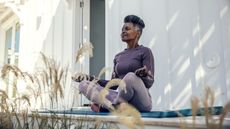 A woman sitting outside on her deck meditates.