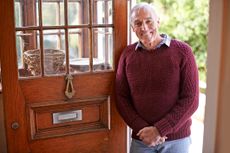 An older, fit man stands in the doorway to his home or rental home.