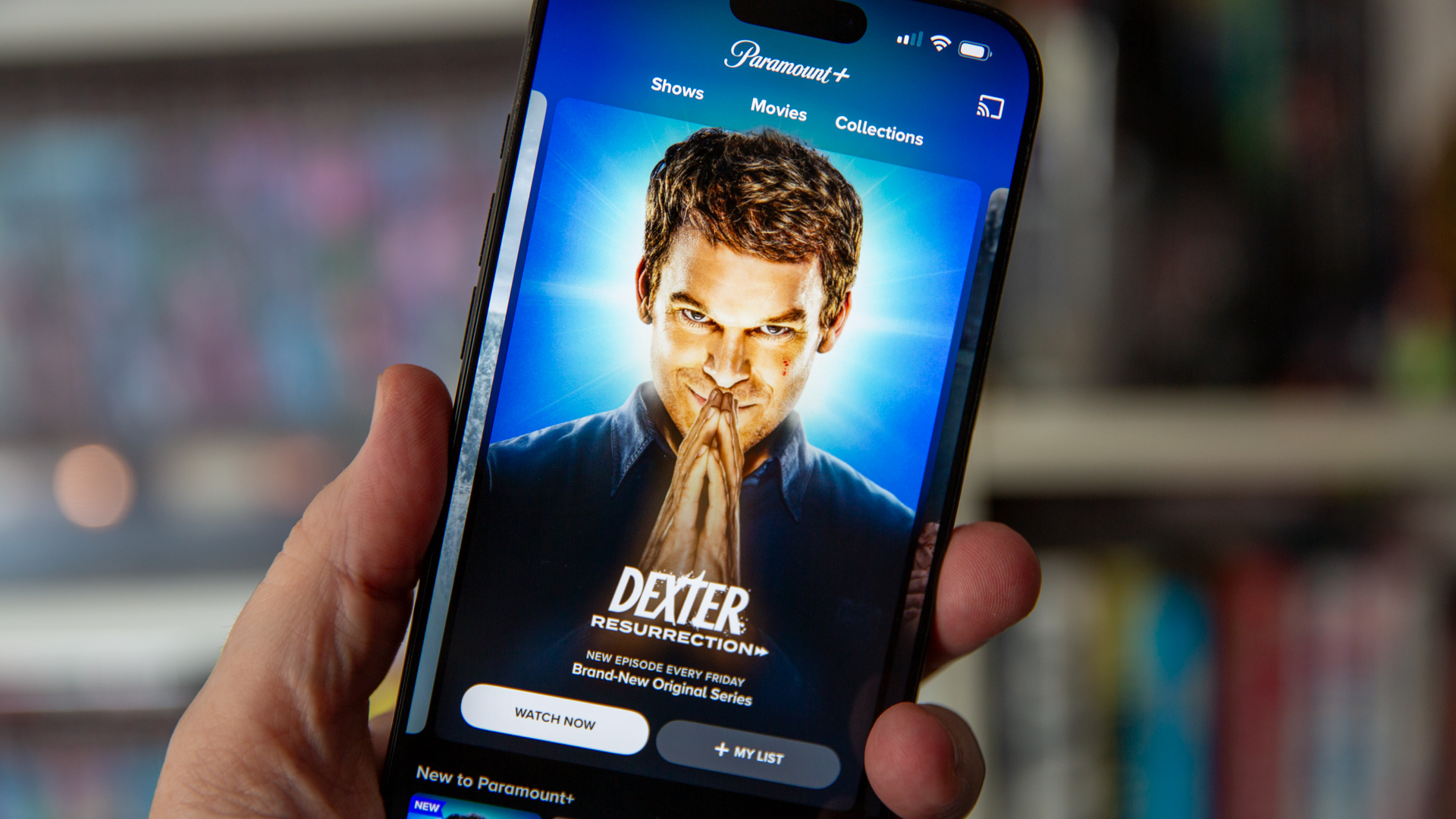 Paramount Plus on an iPhone 16 Pro Max being held in front of book shelves