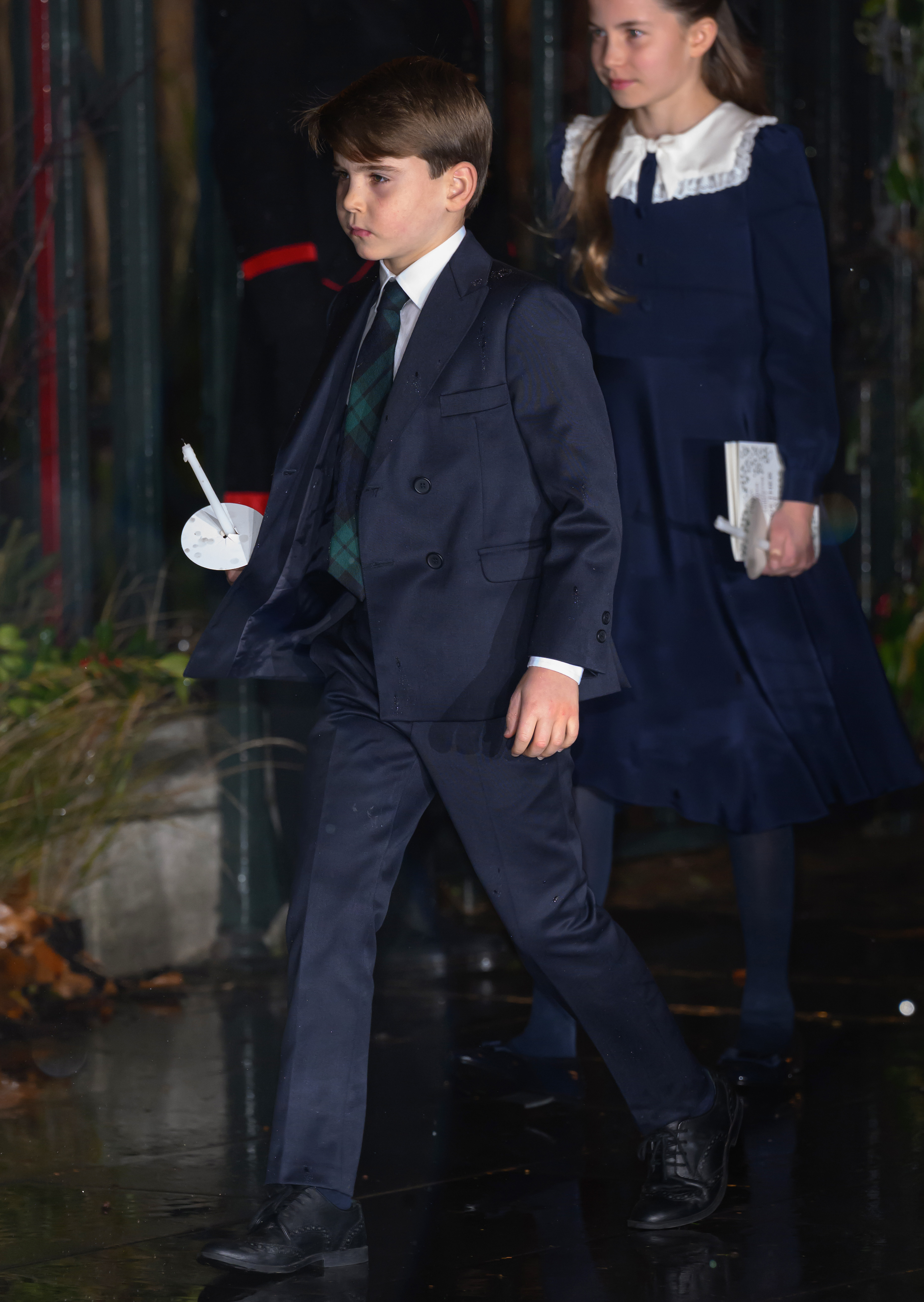 Prince Louis wearing a navy suit walking in front of Princess Charlotte